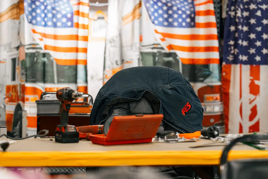 Welding jacket with an FES patch and hand tools on a workbench in front of an American flag backdrop