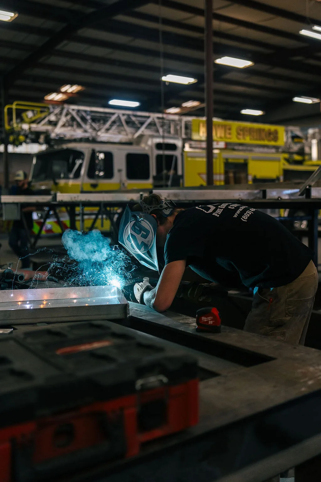 FES welder fabricating aluminum framing with an aerial ladder fire apparatus in the background